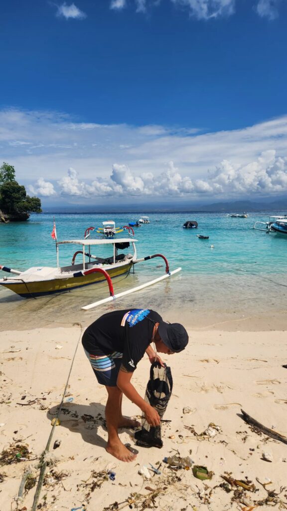 dive instructor viki picking up debris on the beach during the monthly beach clean-up of sca lembongan